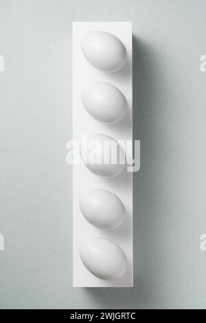Uova di fila su piedistallo bianco su sfondo grigio Foto Stock
