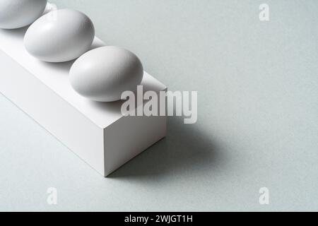 Uova di fila su piedistallo bianco, scatola su sfondo grigio, vista ad angolo alto Foto Stock