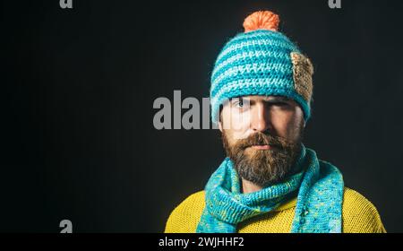 Ritratto ravvicinato di un uomo serio e bello con cappello e sciarpa. Attraente uomo barbuto con cappello, sciarpa e maglione a maglia. Moda autunno-inverno. Elegante Foto Stock