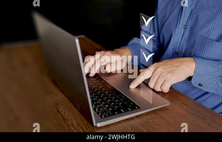 Informazioni sulla lista di controllo. Un uomo con computer portatile controlla i segni digitali corretti sulle caselle di controllo. Monitoraggio intelligente delle prestazioni, compilazione di un sondaggio online, Foto Stock