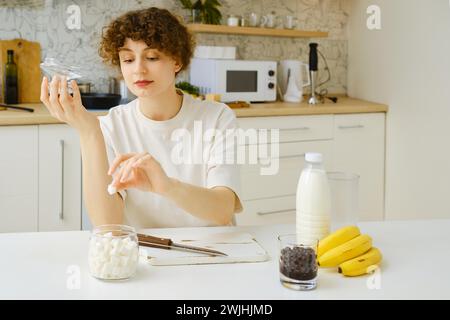 Una donna toglie un pezzo di zucchero da una ciotola mentre è seduta al tavolo della cucina Foto Stock