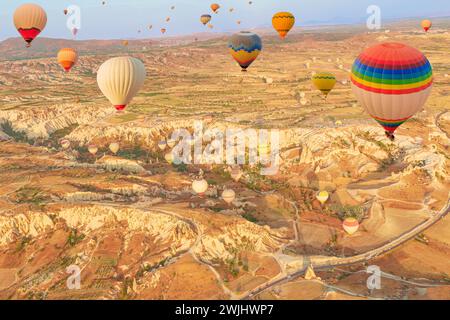 All'alba, una moltitudine di palloncini vibranti della Cappadocia salgono con grazia, proiettando uno spettacolo surreale contro la tranquilla Valle delle Rose di Goreme Foto Stock