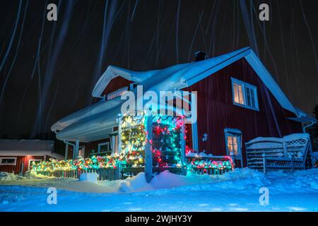 Vista panoramica sulla casa decorata a Natale con molte luci colorate. C'è molta neve sul tetto dopo una forte nevicata. Foto notturna con tracce di neve in caduta Foto Stock