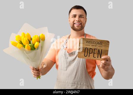 Fiorista maschile che tiene fiori e insegna con testo DI BENVENUTO, SIAMO APERTI su sfondo chiaro Foto Stock