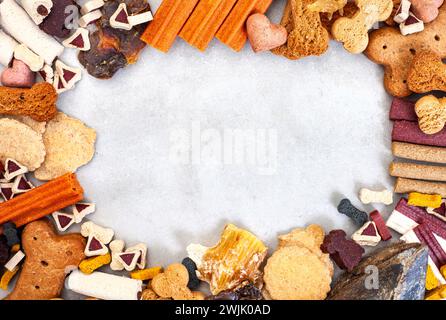 Cornice di dolcetti e masticazioni per cani con spazio di copia. Posizione piatta su grigi a chiazze Foto Stock