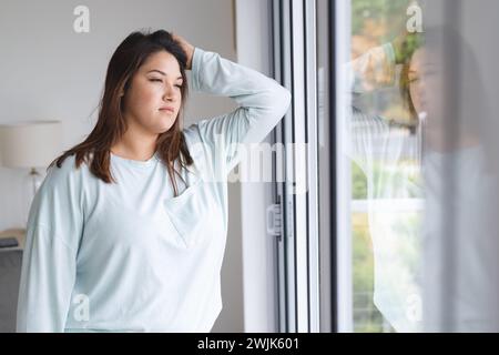 Una giovane donna birazziale più grande sembra contemplativa vicino a una finestra a casa Foto Stock