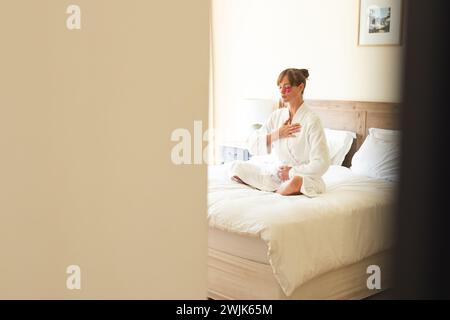 Una donna in accappatoio sta meditando su un letto, con spazio per copiare Foto Stock