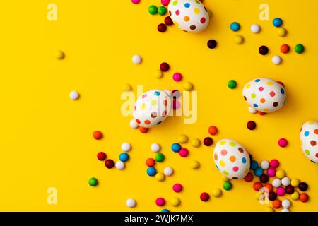 Uova di pasqua colorate macchiate e fagioli di cioccolato colorati su sfondo giallo. Direttamente sopra l'immagine del piano d'esame. Foto Stock