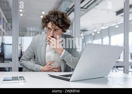 Uomo dai capelli ricci che lavora con attenzione su un notebook in ufficio, trasudando esperienza e concentrazione. Foto Stock