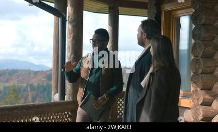 Un agente immobiliare afroamericano professionale con tablet mostra potenziali nuove proprietà per la famiglia con bambini. L'agente immobiliare parla di affittare o acquistare una casa con vista sulle montagne. Foto Stock
