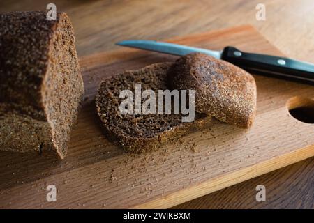 Pane grigio con coltello su tavola di legno. Fette di pane di grano sul tagliere. Prodotti da forno. Pane di segale croccante in tavola. Cena. Foto Stock