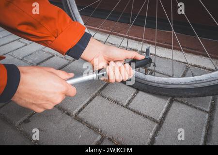 L'uomo prepara la sua bici da strada per la stagione. Soffiare fuori il tubo interno della moto con una pompa per bicicletta manuale. Sport all'aperto. Manutenzione regolare. Foto Stock