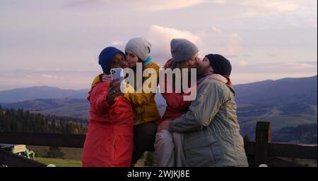 Gli amici dell'escursionismo si trovano vicino a una recinzione di legno e guardano il tramonto. Gruppi di turisti e viaggiatori diversi apprezzano il paesaggio delle montagne e la splendida natura durante il viaggio. Appassionati di attività all'aria aperta. Al rallentatore. Foto Stock