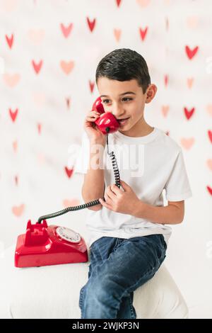 Ragazzo che parla su un telefono rotante con cavo sullo sfondo del cuore Foto Stock