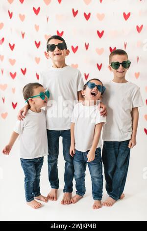 Bambini allegri che indossano occhiali da sole a forma di cuore sullo sfondo del cuore Foto Stock