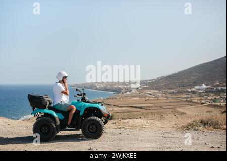 Giovane uomo che regola il casco su un quad a quattro ruote dal paesaggio costiero Foto Stock