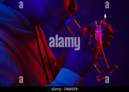 uomo afroamericano corto in bong di vetro con cappuccio su sfondo blu scuro con luce rossa Foto Stock