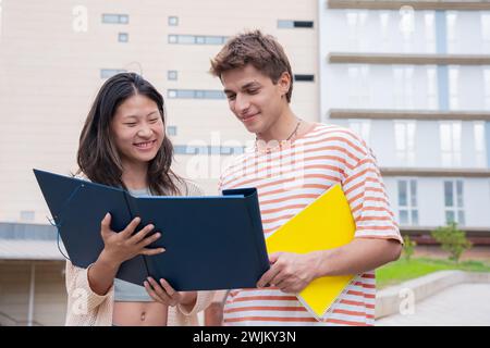 Amici sorridenti del college che guardano appunti, parlano e ridono nel campus. Foto Stock