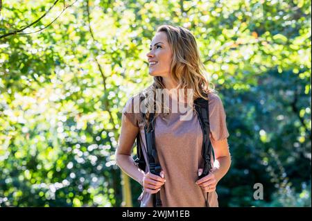 Bella donna che indossa lo zaino mentre cammina nel bosco Foto Stock