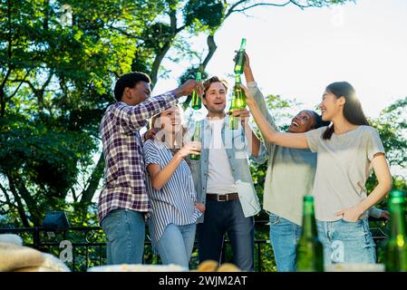 Cinque amici che allevano bottiglie di birra mentre brindano durante la festa sul tetto Foto Stock
