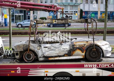 Lipsia, Germania. 16 febbraio 2024. Una BMW Z3 bruciata si trova su un rimorchio dopo essere stata salvata dal parcheggio sotterraneo di Augustusplatz. Il dipartimento investigativo sta indagando su un incendio nel parcheggio sotterraneo sotto Augustusplatz di Lipsia. Durante la notte, due auto sono state completamente distrutte nell'incendio e un'altra auto e un furgone sono stati danneggiati. Il parcheggio sotterraneo sul lato dell'Opera rimane chiuso fino a quando un ingegnere strutturale non lo ha ispezionato. Crediti: Jan Woitas/dpa/Alamy Live News Foto Stock