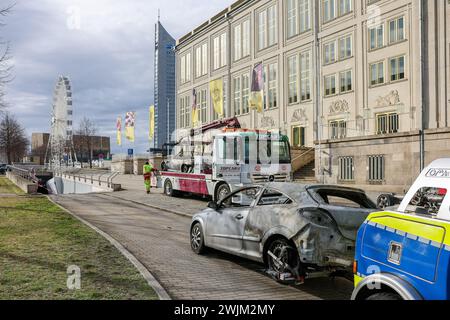 Lipsia, Germania. 16 febbraio 2024. I dipendenti di un'azienda di traino recuperano una Opel Astra danneggiata e una BMW Z3 bruciata dal parcheggio sotterraneo di Augustusplatz dopo un incendio. Il dipartimento investigativo sta indagando su un incendio nel parcheggio sotterraneo sotto Augustusplatz di Lipsia. Durante la notte, due auto sono state completamente distrutte nell'incendio e un'altra auto e un furgone sono stati danneggiati. Il parcheggio sotterraneo sul lato dell'Opera rimane chiuso fino a quando un ingegnere strutturale non lo ha ispezionato. Crediti: Jan Woitas/dpa/Alamy Live News Foto Stock