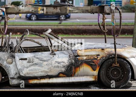 Lipsia, Germania. 16 febbraio 2024. Una BMW Z3 bruciata si trova su un rimorchio dopo essere stata salvata dal parcheggio sotterraneo di Augustusplatz. Il dipartimento investigativo sta indagando su un incendio nel parcheggio sotterraneo sotto Augustusplatz di Lipsia. Durante la notte, due auto sono state completamente distrutte nell'incendio e un'altra auto e un furgone sono stati danneggiati. Il parcheggio sotterraneo sul lato dell'Opera rimane chiuso fino a quando un ingegnere strutturale non lo ha ispezionato. Crediti: Jan Woitas/dpa/Alamy Live News Foto Stock