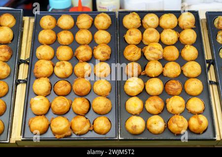 Un venditore ambulante in azione, che prepara Takoyaki, un popolare spuntino giapponese a base di polpo grigliato, guarnito con condimento Foto Stock