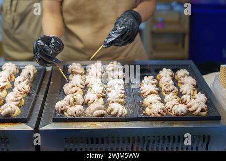 Un venditore ambulante in azione, che prepara Takoyaki, un popolare spuntino giapponese a base di polpo grigliato, guarnito con condimento Foto Stock