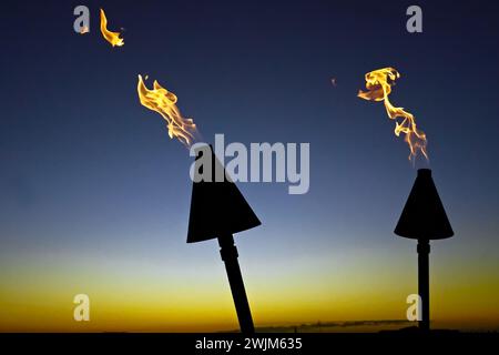 Hawaii, isola polinesiana del Pacifico, moderne fiamme di torcia tiki alimentate a gas naturale al tramonto presso il resort tropicale sulla spiaggia Foto Stock