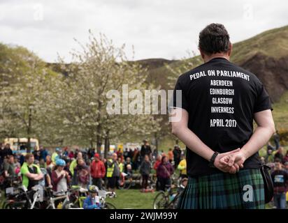 Un uomo con una maglietta dimostrativa affronta centinaia di ciclisti e persone con le biciclette fuori dal Parlamento che hanno pedalato per le strade di Edimburgo per andare da professionista Foto Stock