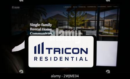 Persona che possiede un telefono cellulare con il logo della società immobiliare canadese Tricon Residential Inc. Di fronte alla pagina web. Mettere a fuoco il display del telefono. Foto Stock