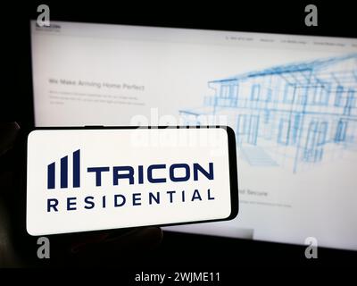 Persona che detiene un cellulare con il logo della società immobiliare canadese Tricon Residential Inc. Di fronte alla pagina web aziendale. Mettere a fuoco il display del telefono. Foto Stock