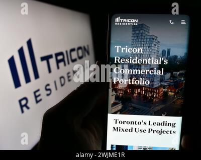 Persona che detiene un cellulare con pagina web della società immobiliare canadese Tricon Residential Inc. Davanti al logo. Messa a fuoco al centro del display del telefono. Foto Stock