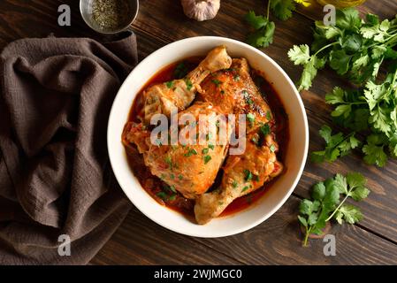 Stufato di pollo georgiano con pomodori ed erbe (chakhokhbili) in una ciotola su fondo di legno. Carne di pollo al forno con sugo di verdure al pomodoro. Sana e Foto Stock