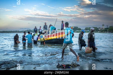 I facchini si affrettano a scaricare i sacchi di acciuga da un tradizionale dhow di legno affollato di pescatori dopo che arrivano in serata al Kivukoni Fish Foto Stock