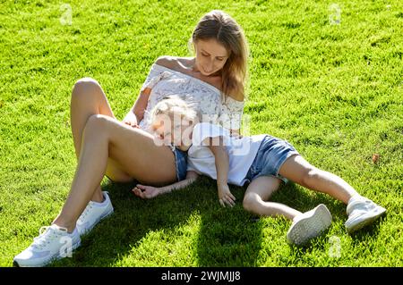 Madre con figlia sdraiata sul prato nel parco cittadino estivo. Concetto di infanzia, tempo libero e persone - buon riposo in famiglia e buon divertimento Foto Stock