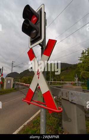 Segnaletica stradale rossa e bianca per attraversamento ferroviario con a. luce rossa di arresto di fronte a un paesaggio verde e un cielo grigio Foto Stock