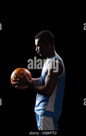 Uomo afroamericano che regge una pallacanestro su sfondo nero Foto Stock