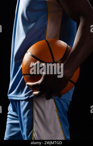Uomo afroamericano che regge una pallacanestro su sfondo nero Foto Stock