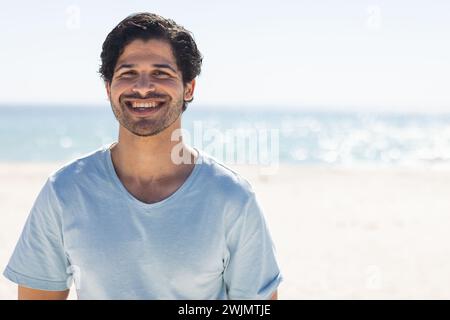 Il giovane uomo birazziale sorride brillantemente in spiaggia Foto Stock
