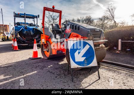 Un rullo, parcheggiato sul lato della strada, viene utilizzato per compattare materiale durante la riparazione o la posa di nuove strade. Foto Stock