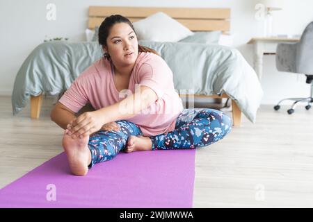 Una giovane donna birazziale più grande si allunga su un tappetino da yoga a casa Foto Stock