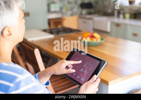 Una donna birazziale matura che usa un tablet nella sua cucina di casa Foto Stock