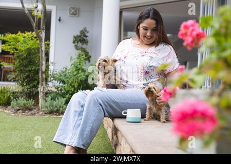 Una giovane donna birazziale più grande ama passare il tempo libero con i cani in un giardino di casa Foto Stock