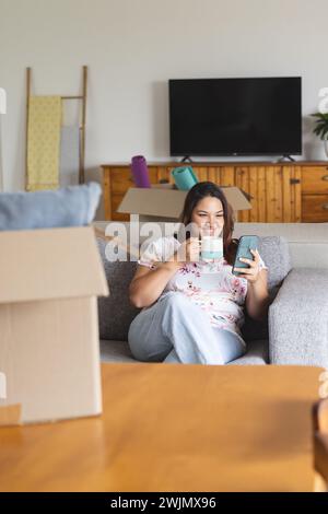 Una giovane donna birazziale di grandi dimensioni si gode una pausa a casa, circondata da scatole mobili Foto Stock