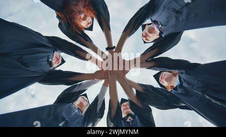 Team di studenti universitari o universitari che celebrano la laurea. Gruppo di laureati felici e di successo in cappelli e vesti accademici in piedi in cerchio e. Foto Stock