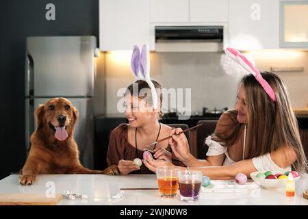 Mamma e figlia stanno decorando le uova di Pasqua con un cane Golden retriever. Foto Stock