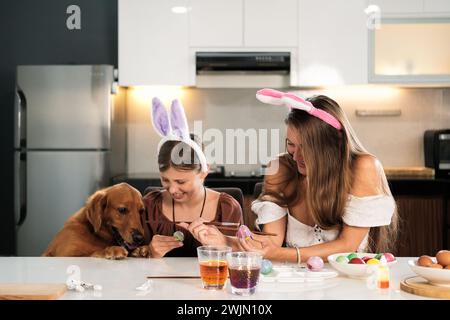 Mamma e figlia stanno decorando le uova di Pasqua con un cane Golden retriever. Foto Stock