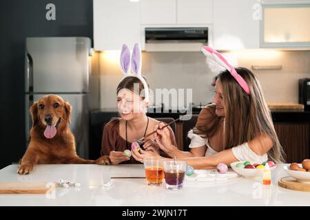 Mamma e figlia stanno decorando le uova di Pasqua con un cane Golden retriever. Foto Stock